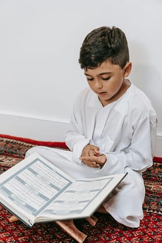 pexels-photo-9127846-9127846 A young boy dressed in white reads the Quran, symbolizing cultural and religious devotion.